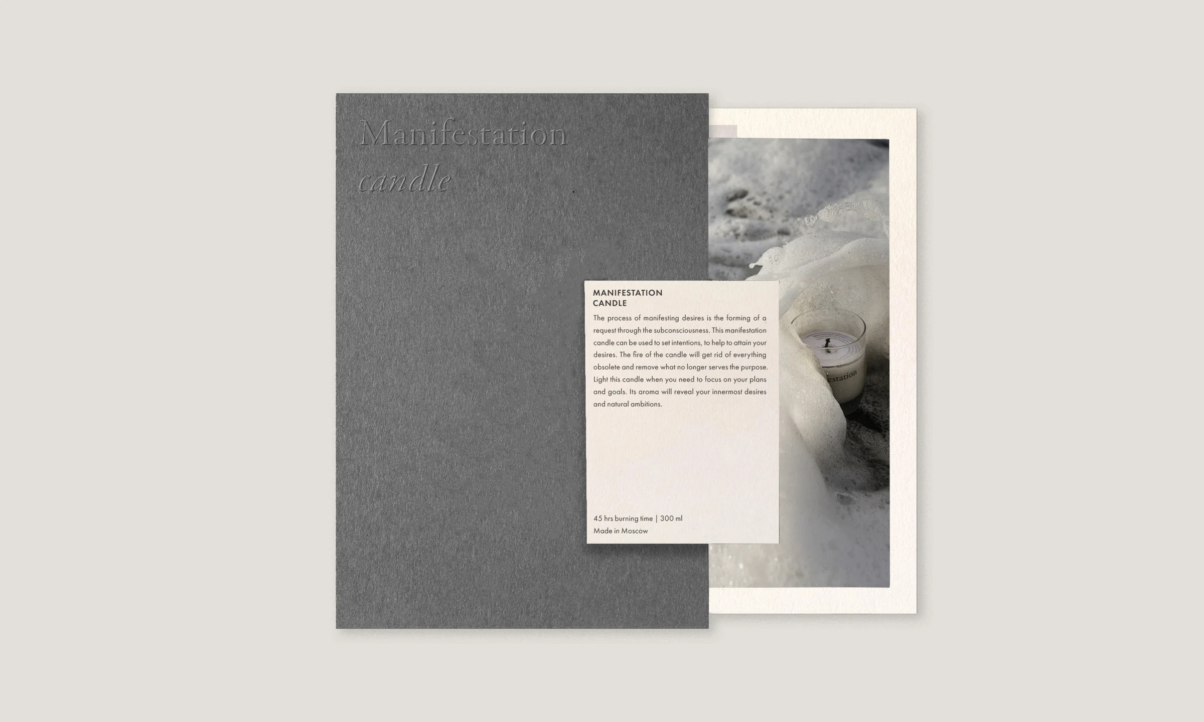 Grey embossed folder with a product card and photo print of a lit candle in white wax, for Manifestation Candles.