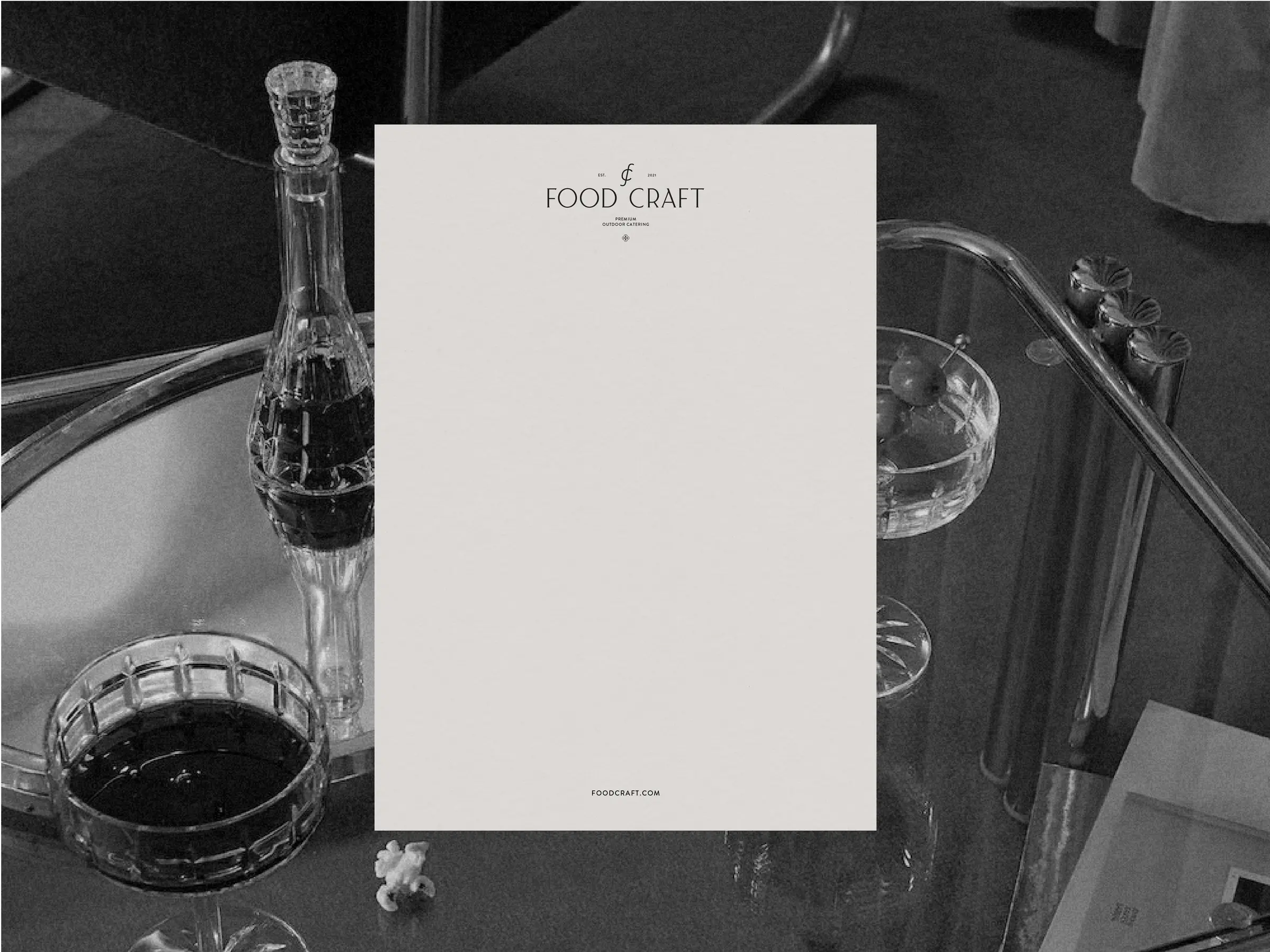 Cream letterhead with serif wordmark over a black-and-white glass bar cart with crystal decanter and coupes, for Food Craft.