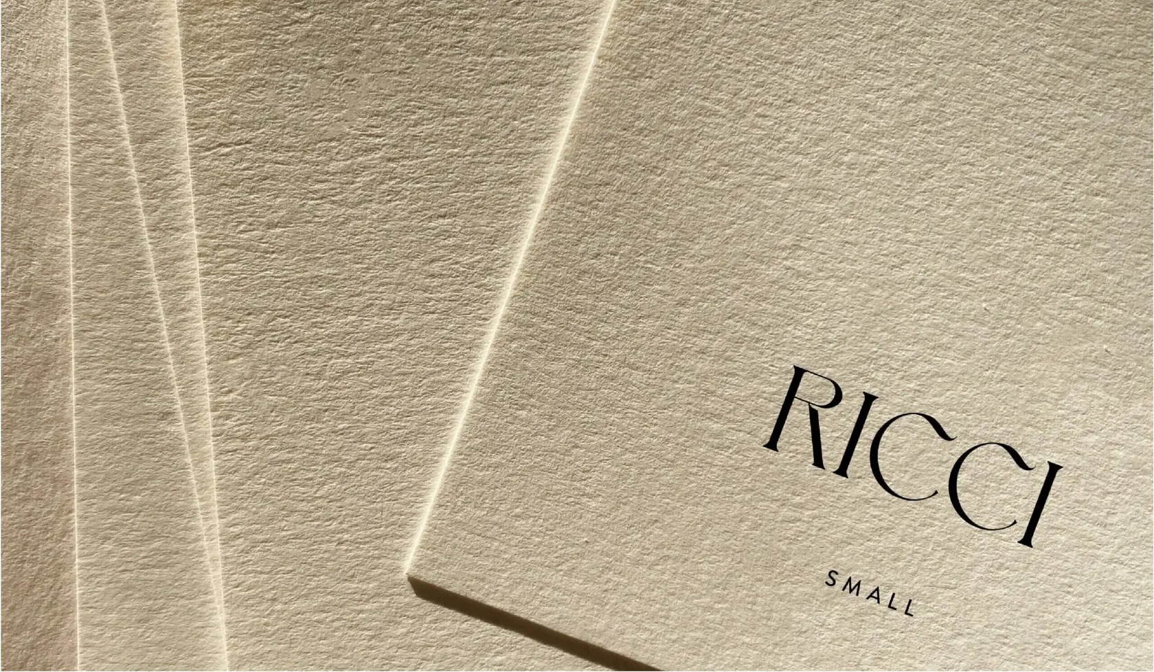 Stack of textured cream cotton cards printed with the RICCI Small wordmark in black, for Ricci.