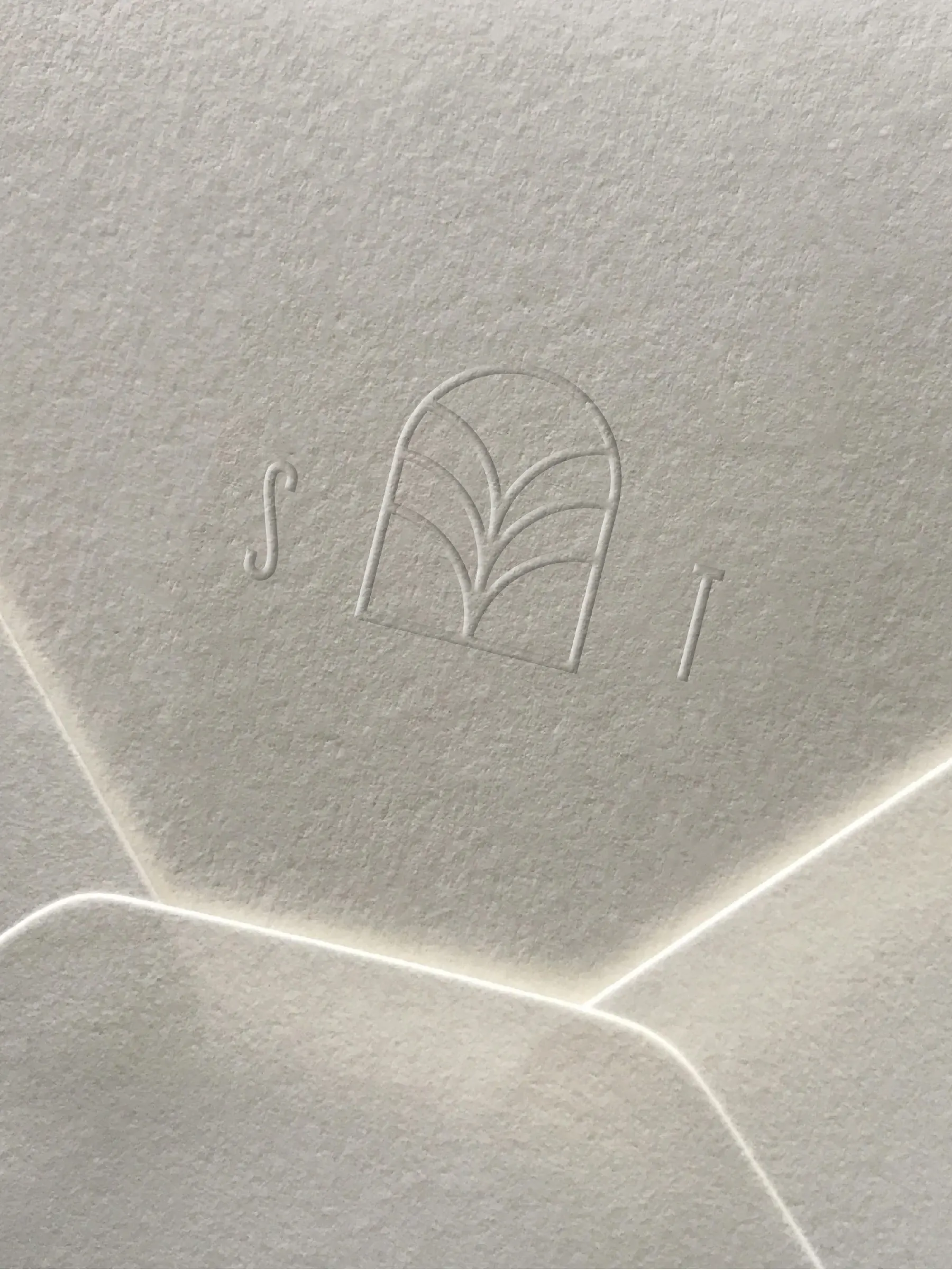 Blind-embossed S T monogram with arched leaf emblem on textured off-white envelope paper, for Stone Temple.