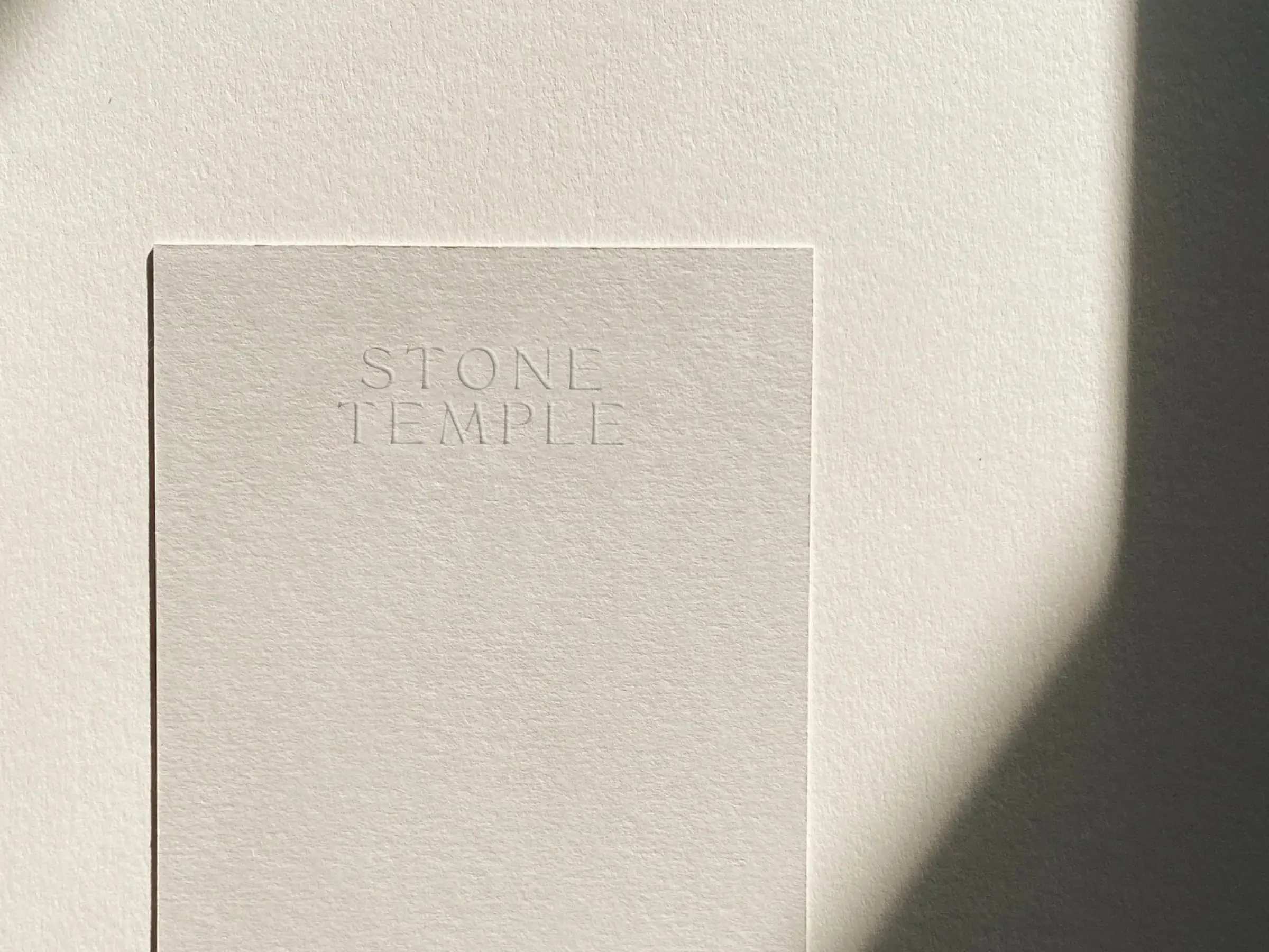 Cream textured card with a blind-embossed serif wordmark, lit by soft window light and shadow, for Stone Temple.