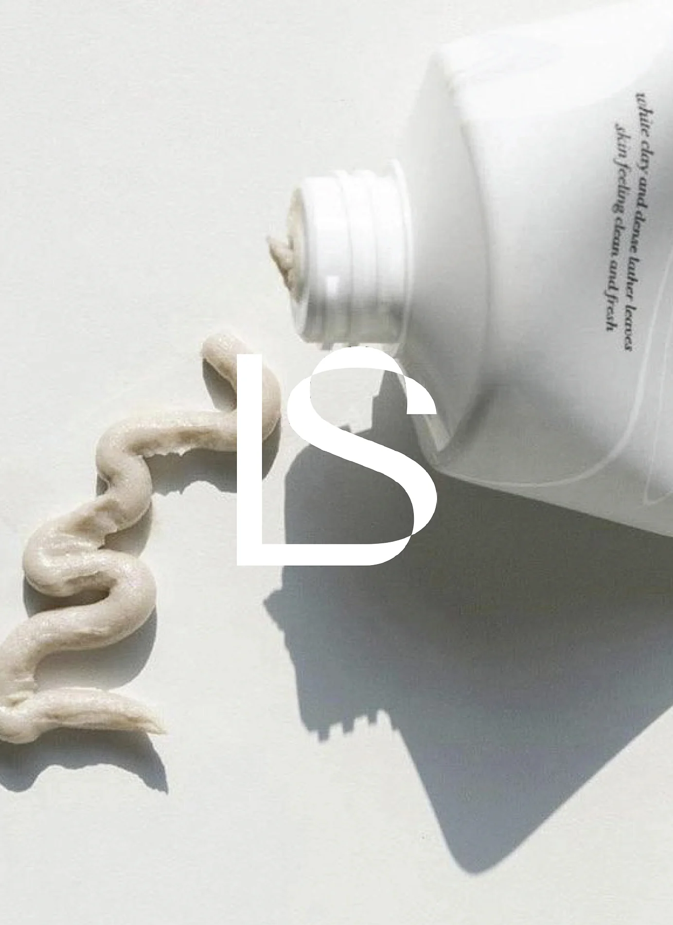 White tube squeezing a swirl of beige clay cleanser on white, overlaid with a white LS monogram, for Lightsaver.