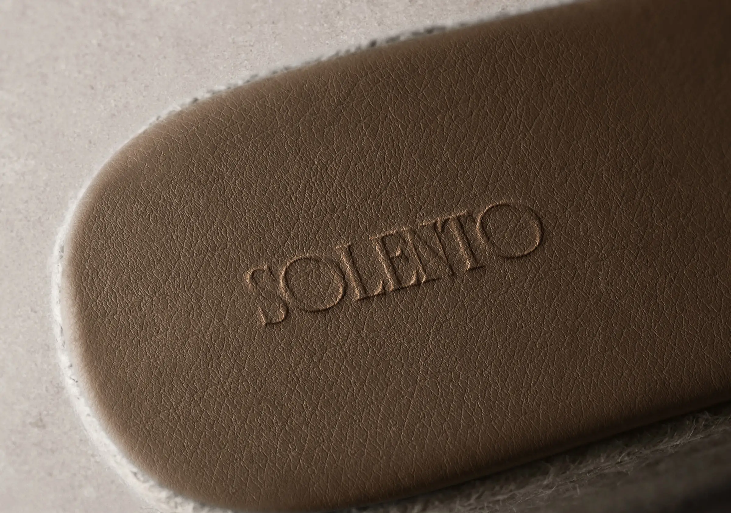 Brown leather shoe insole debossed with the Solento wordmark, resting on a grey felt surface, for Solento.