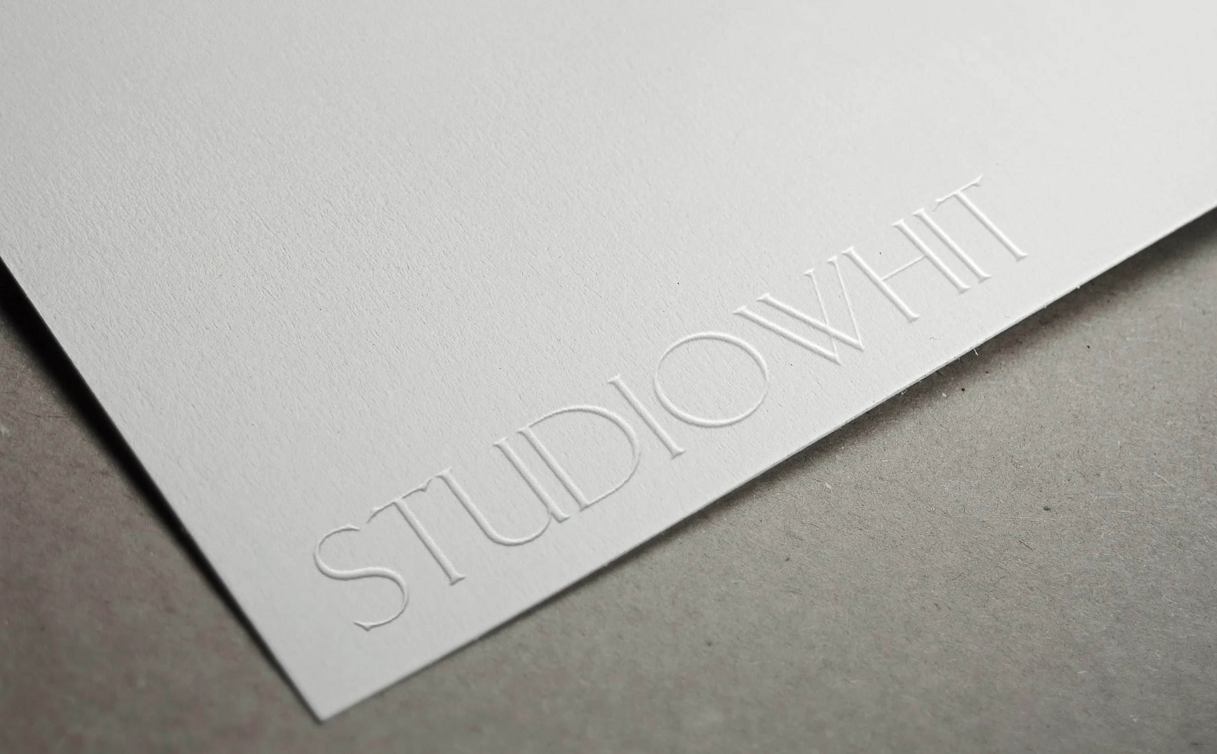 Wordmark blind embossed on textured white paper resting on a grey surface, for Studio Whit.