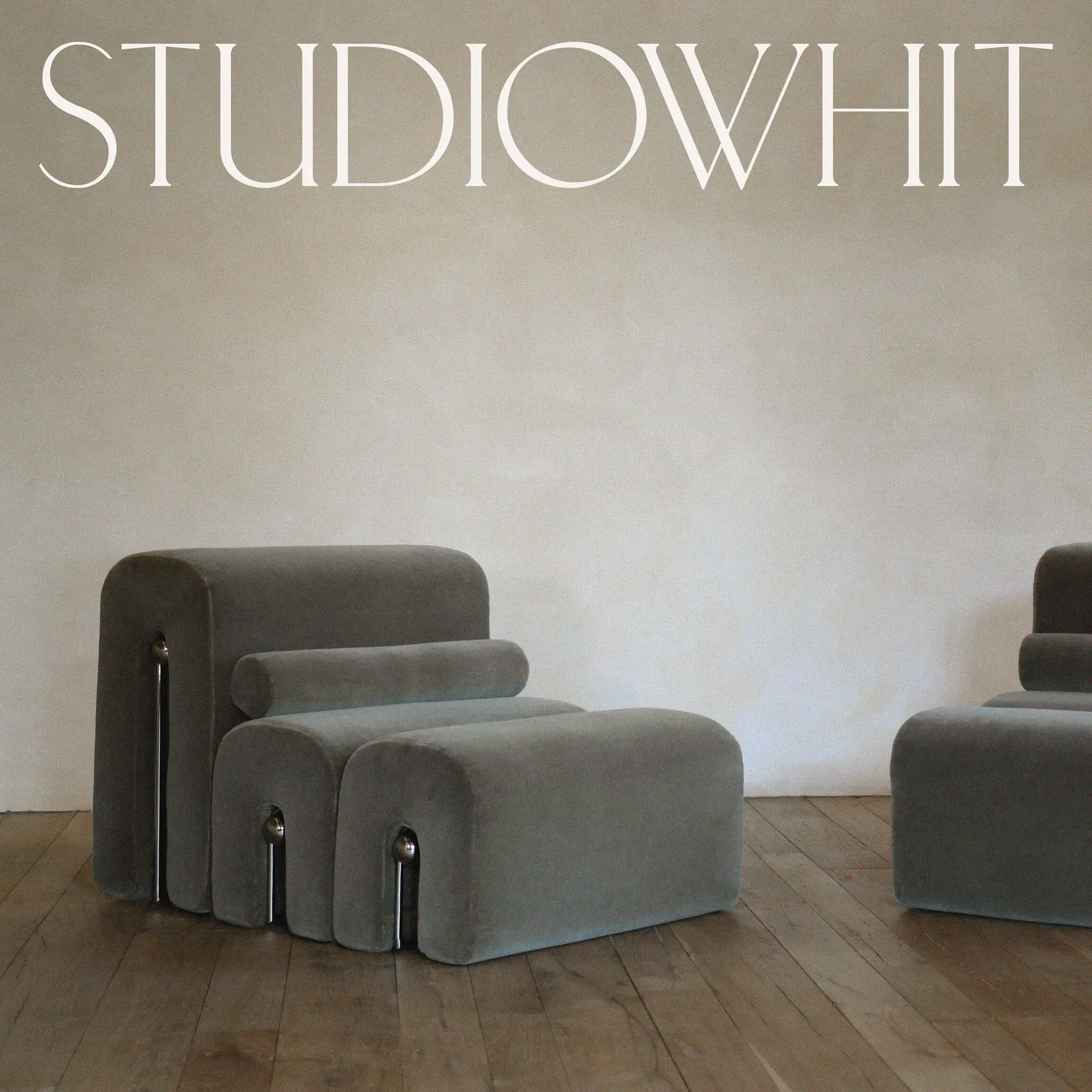 Grey velvet modular lounge chair with chrome legs on a wooden floor, under a white wordmark, for Studio Whit.